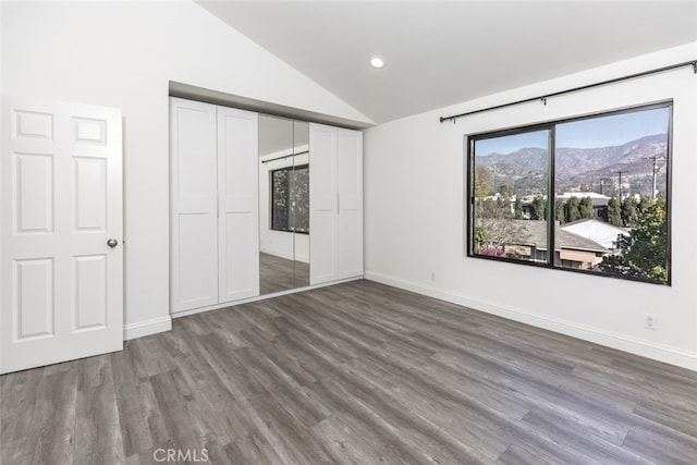 unfurnished bedroom featuring a closet, vaulted ceiling, a mountain view, and wood-type flooring