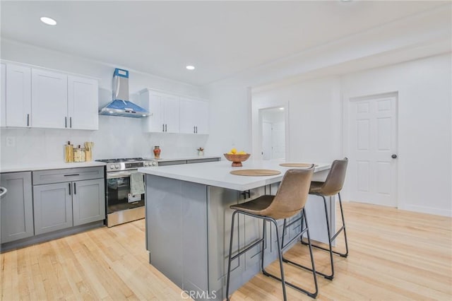 kitchen with wall chimney range hood, a kitchen bar, a kitchen island, white cabinets, and stainless steel range with gas stovetop