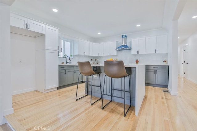 kitchen with light wood-type flooring, a breakfast bar, a kitchen island, wall chimney range hood, and tasteful backsplash