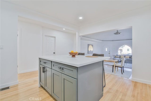 kitchen with gray cabinets, light hardwood / wood-style floors, a kitchen breakfast bar, and a center island