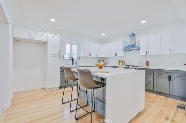 kitchen with a kitchen island, white cabinets, wall chimney exhaust hood, and light hardwood / wood-style flooring