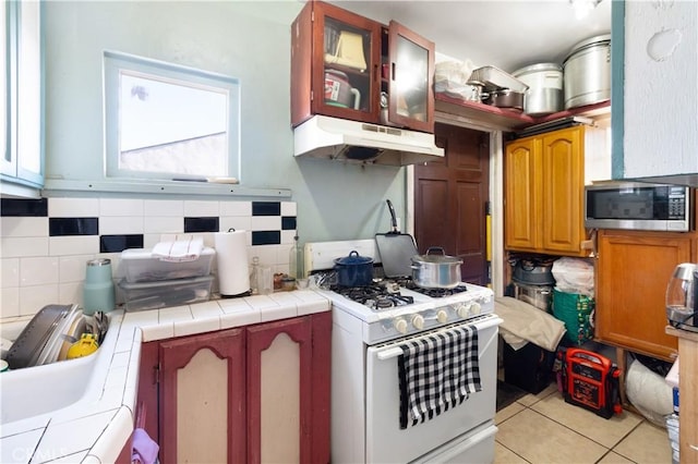 kitchen with decorative backsplash, tile counters, white gas stove, and light tile patterned flooring