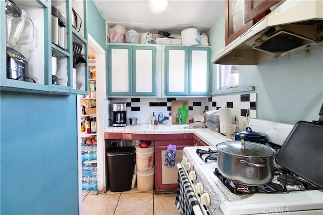 kitchen featuring gas range gas stove, tile counters, light tile patterned floors, and decorative backsplash