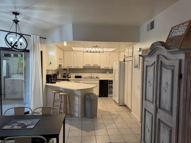 kitchen featuring white refrigerator, pendant lighting, washer / dryer, white cabinets, and an inviting chandelier