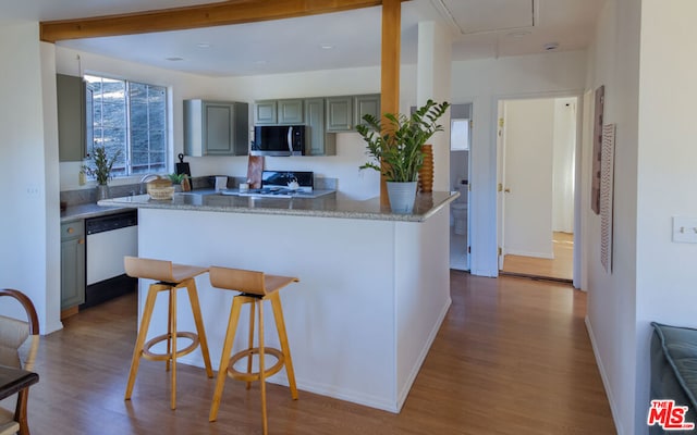 kitchen featuring stainless steel appliances, hardwood / wood-style flooring, kitchen peninsula, gray cabinets, and a breakfast bar