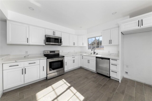 kitchen featuring sink, white cabinets, light stone counters, and appliances with stainless steel finishes