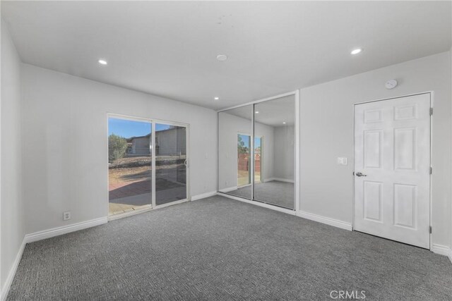 unfurnished bedroom featuring a closet, dark carpet, and access to exterior