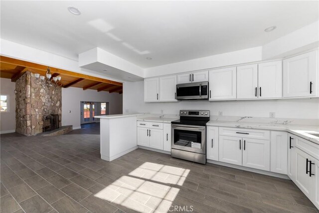 kitchen with a chandelier, appliances with stainless steel finishes, vaulted ceiling with beams, kitchen peninsula, and white cabinets