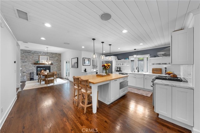 kitchen featuring wood ceiling, a stone fireplace, a center island, wood counters, and white cabinets