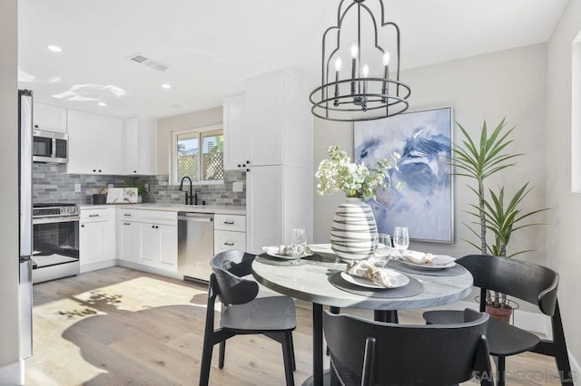 dining space with sink, light wood-type flooring, and a chandelier