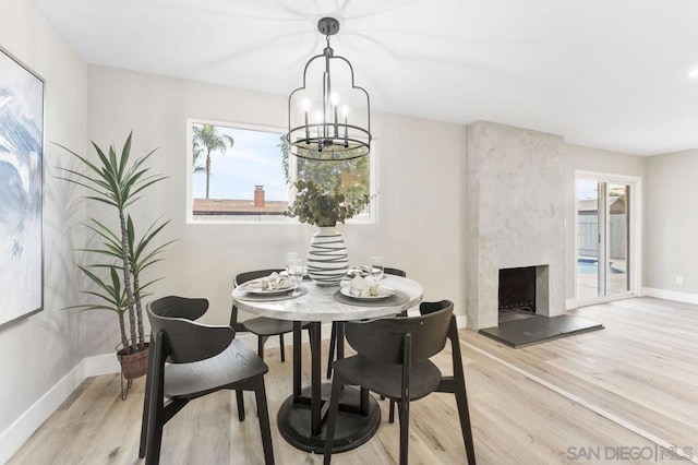 dining space with a high end fireplace, an inviting chandelier, and light hardwood / wood-style floors