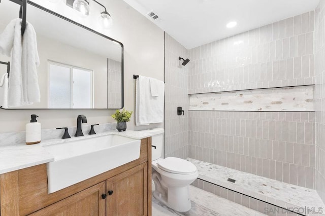 bathroom featuring toilet, vanity, and tiled shower