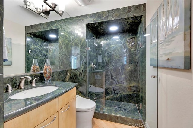 bathroom featuring toilet, tiled shower, tile walls, and vanity