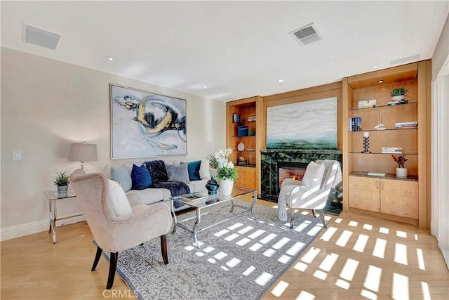 living room featuring light hardwood / wood-style floors, a premium fireplace, and built in features