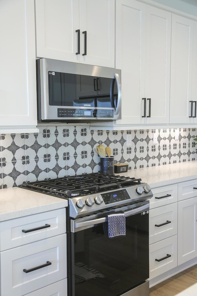 kitchen with stainless steel appliances, white cabinets, light stone counters, light hardwood / wood-style floors, and backsplash