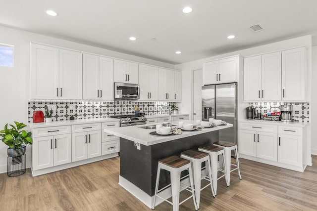 kitchen with stainless steel appliances, a breakfast bar, a kitchen island with sink, white cabinets, and sink