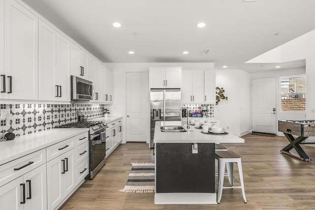 kitchen with stainless steel appliances, sink, white cabinets, light hardwood / wood-style floors, and a center island with sink