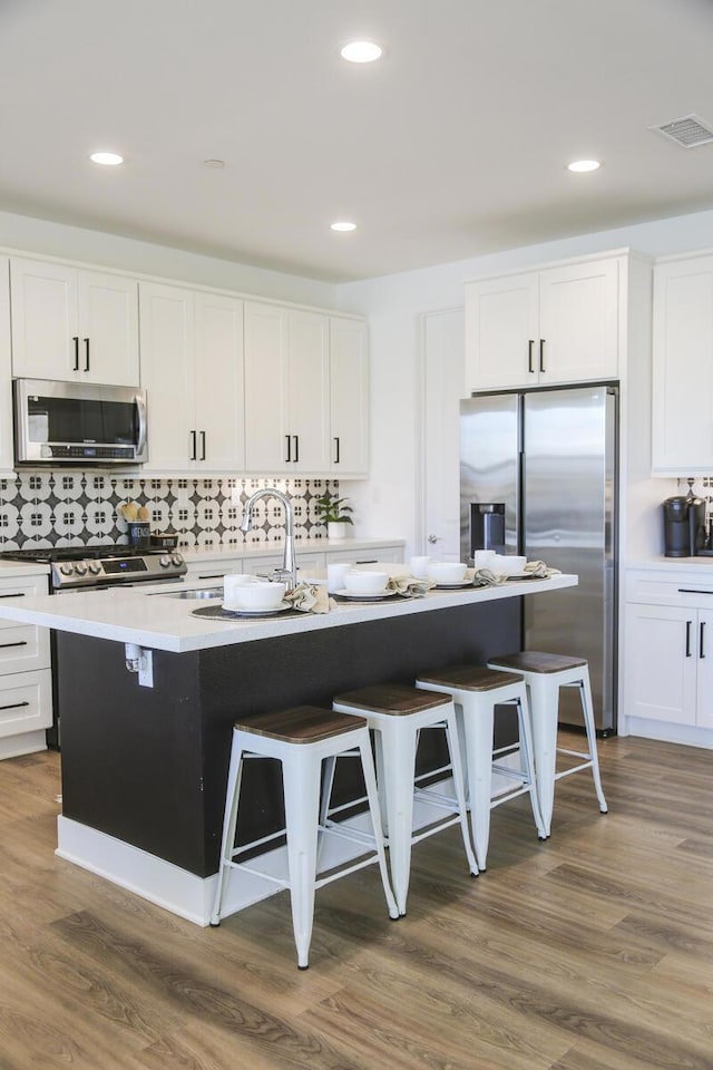 kitchen with a breakfast bar area, dark hardwood / wood-style flooring, an island with sink, and appliances with stainless steel finishes