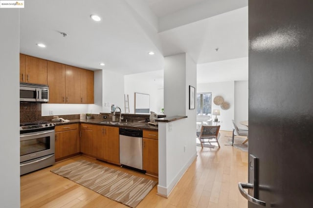 kitchen with stainless steel appliances, sink, light hardwood / wood-style floors, tasteful backsplash, and kitchen peninsula