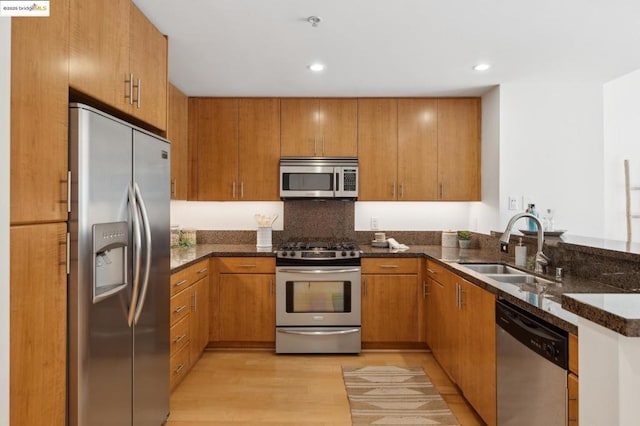 kitchen with stainless steel appliances, sink, light wood-type flooring, and dark stone counters