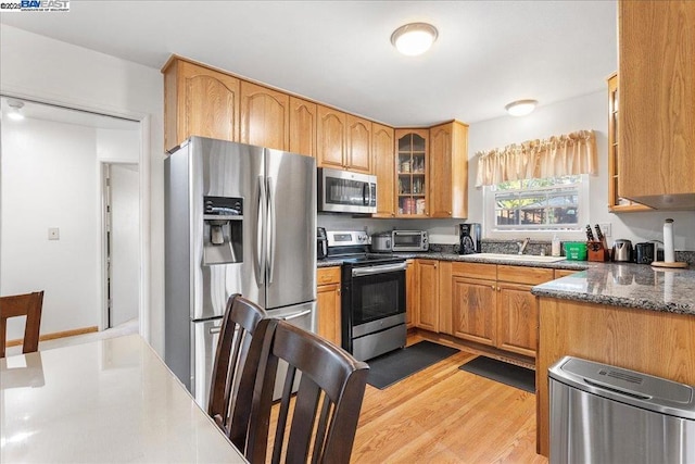 kitchen with stainless steel appliances, sink, dark stone countertops, and light hardwood / wood-style floors