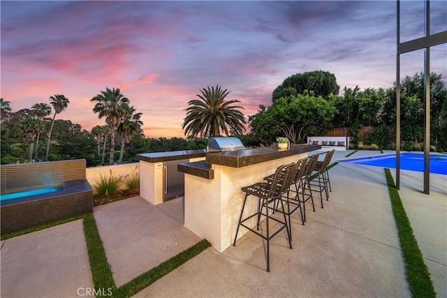 patio terrace at dusk featuring an outdoor kitchen, a grill, and exterior bar