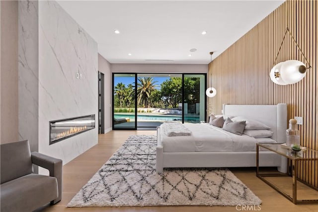 bedroom featuring access to exterior, a tiled fireplace, and light hardwood / wood-style flooring