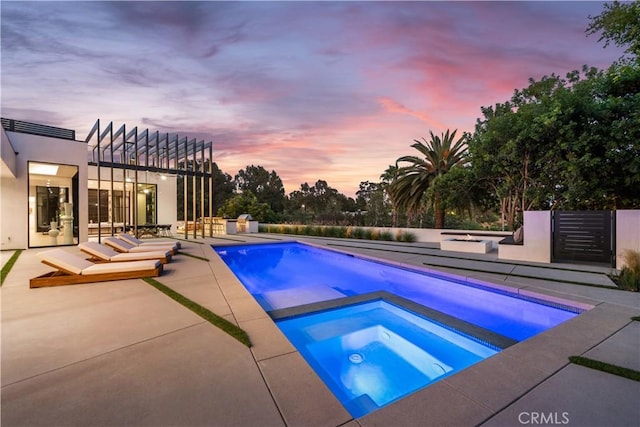 pool at dusk with an in ground hot tub and a patio