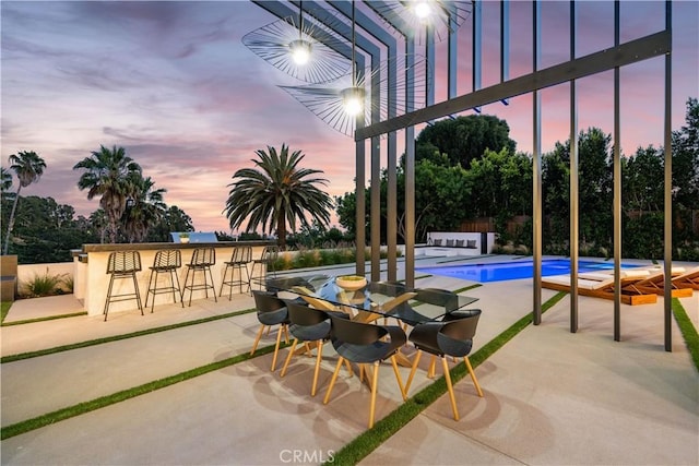 patio terrace at dusk with a fenced in pool and a bar