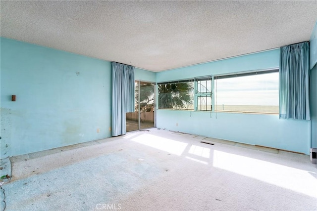 unfurnished room featuring a textured ceiling, carpet, plenty of natural light, and visible vents