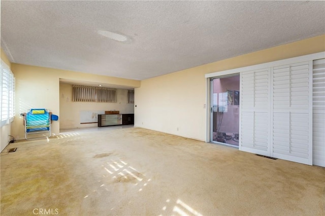unfurnished living room with a textured ceiling, carpet floors, and visible vents