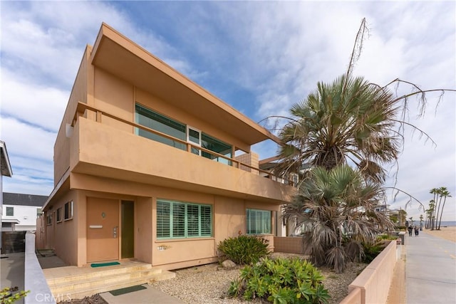 view of side of property with stucco siding, fence, and a balcony