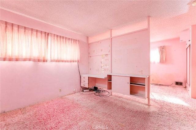 unfurnished bedroom featuring carpet flooring, built in study area, visible vents, and a textured ceiling