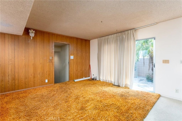 carpeted empty room with wood walls and a textured ceiling