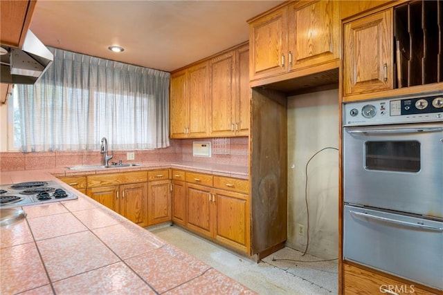 kitchen featuring wall oven, a sink, tile counters, stainless steel electric stovetop, and a warming drawer