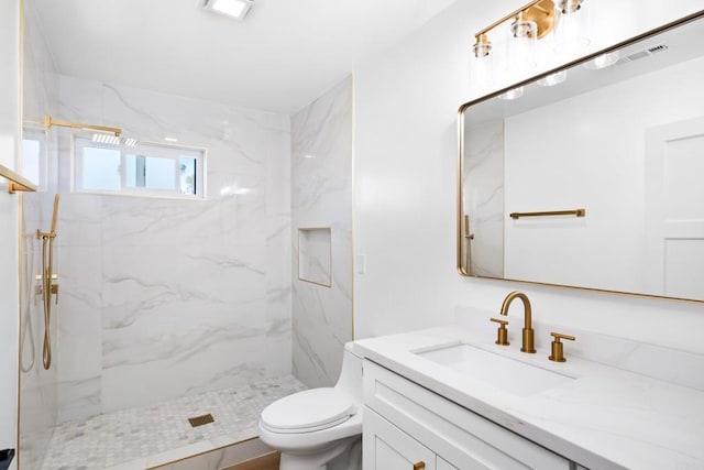 bathroom featuring a tile shower, vanity, and toilet