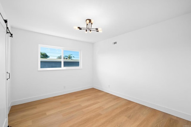 spare room featuring a notable chandelier, light hardwood / wood-style floors, and a barn door