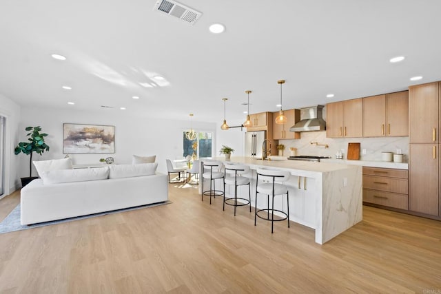 kitchen with a spacious island, wall chimney exhaust hood, light hardwood / wood-style floors, and light brown cabinets