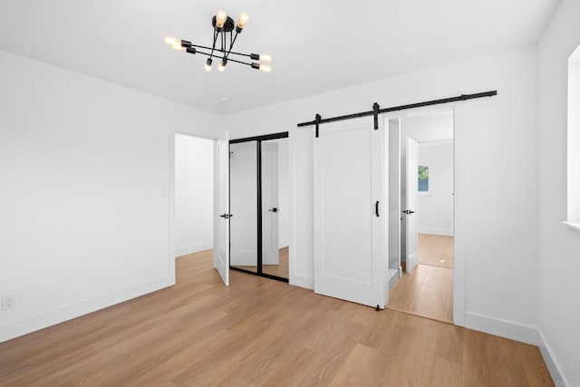 unfurnished bedroom with light hardwood / wood-style flooring, an inviting chandelier, and a barn door