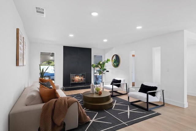 living room featuring a tile fireplace, ceiling fan, and light hardwood / wood-style floors