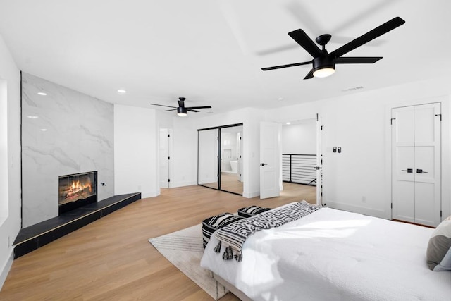 bedroom featuring ceiling fan, light hardwood / wood-style floors, two closets, and a fireplace