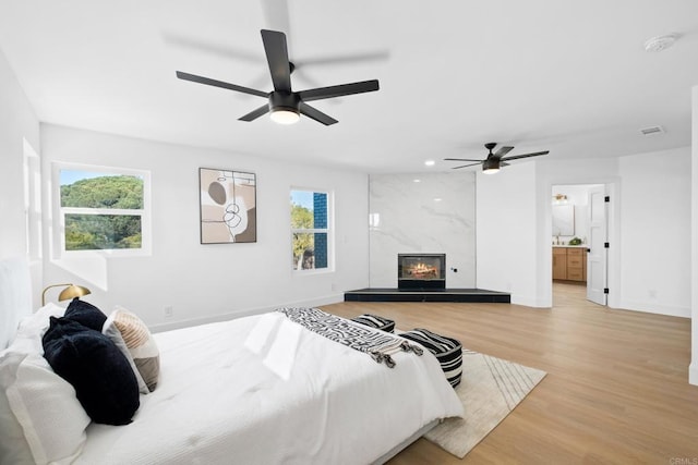 bedroom featuring ensuite bathroom, a premium fireplace, ceiling fan, and light hardwood / wood-style floors