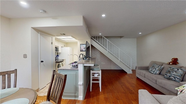 kitchen featuring a textured ceiling, stainless steel appliances, dark hardwood / wood-style flooring, a breakfast bar area, and white cabinets