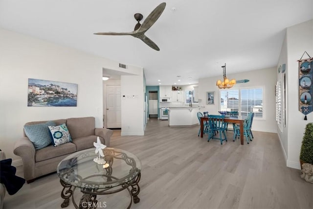 living room with ceiling fan with notable chandelier and light hardwood / wood-style flooring