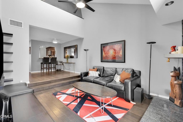 living room with a high ceiling, dark wood-type flooring, and ceiling fan