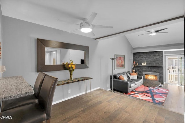 living room featuring ceiling fan, vaulted ceiling, dark hardwood / wood-style floors, and a stone fireplace