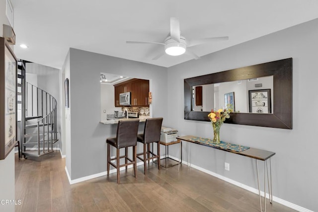 kitchen with wood-type flooring, kitchen peninsula, ceiling fan, a breakfast bar, and decorative backsplash