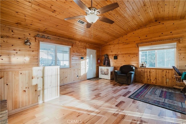 living area with visible vents, wood walls, light wood finished floors, and vaulted ceiling