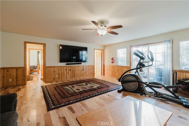 workout area featuring ceiling fan, light wood-type flooring, and wood walls