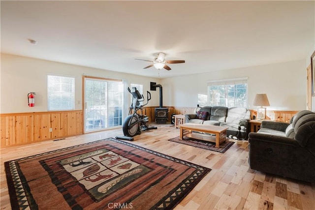 living room featuring ceiling fan, light hardwood / wood-style flooring, a wood stove, and plenty of natural light